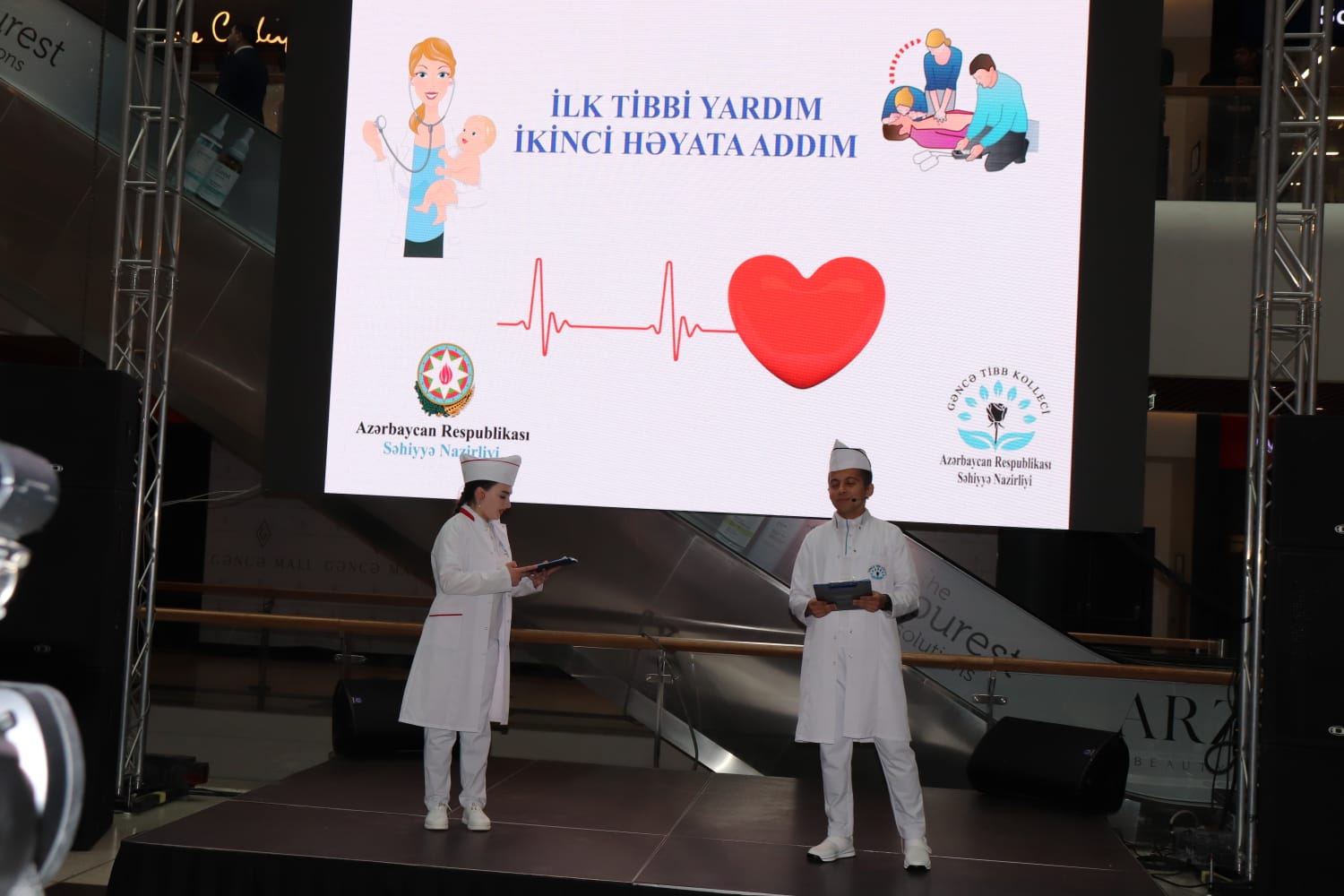 a couple of people in white lab coats standing in front of a large screen