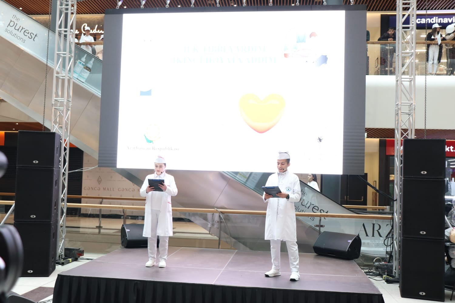 a couple of men in white uniforms on a stage with a projector screen and speakers