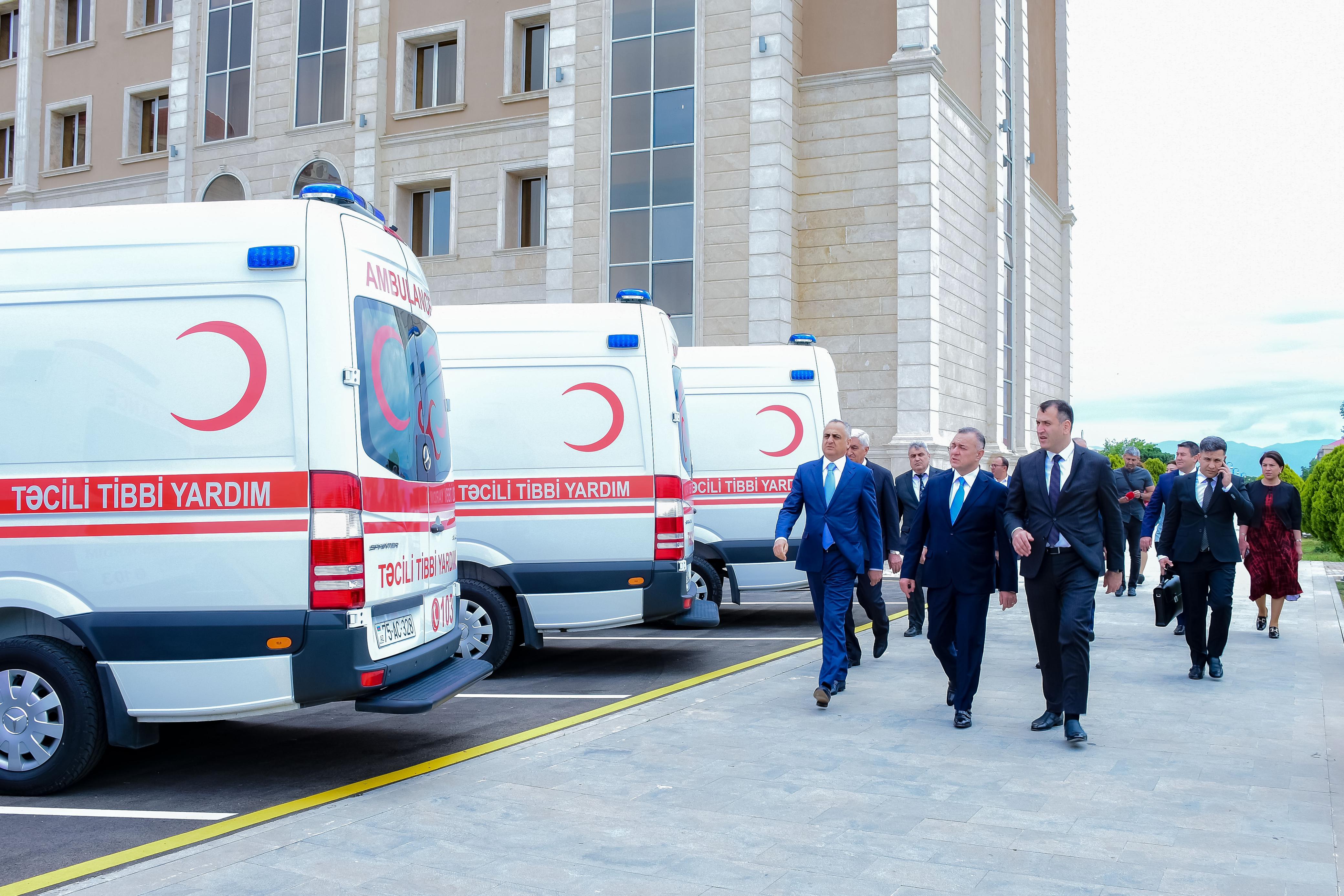 a group of people walking down a street next to a white ambulance