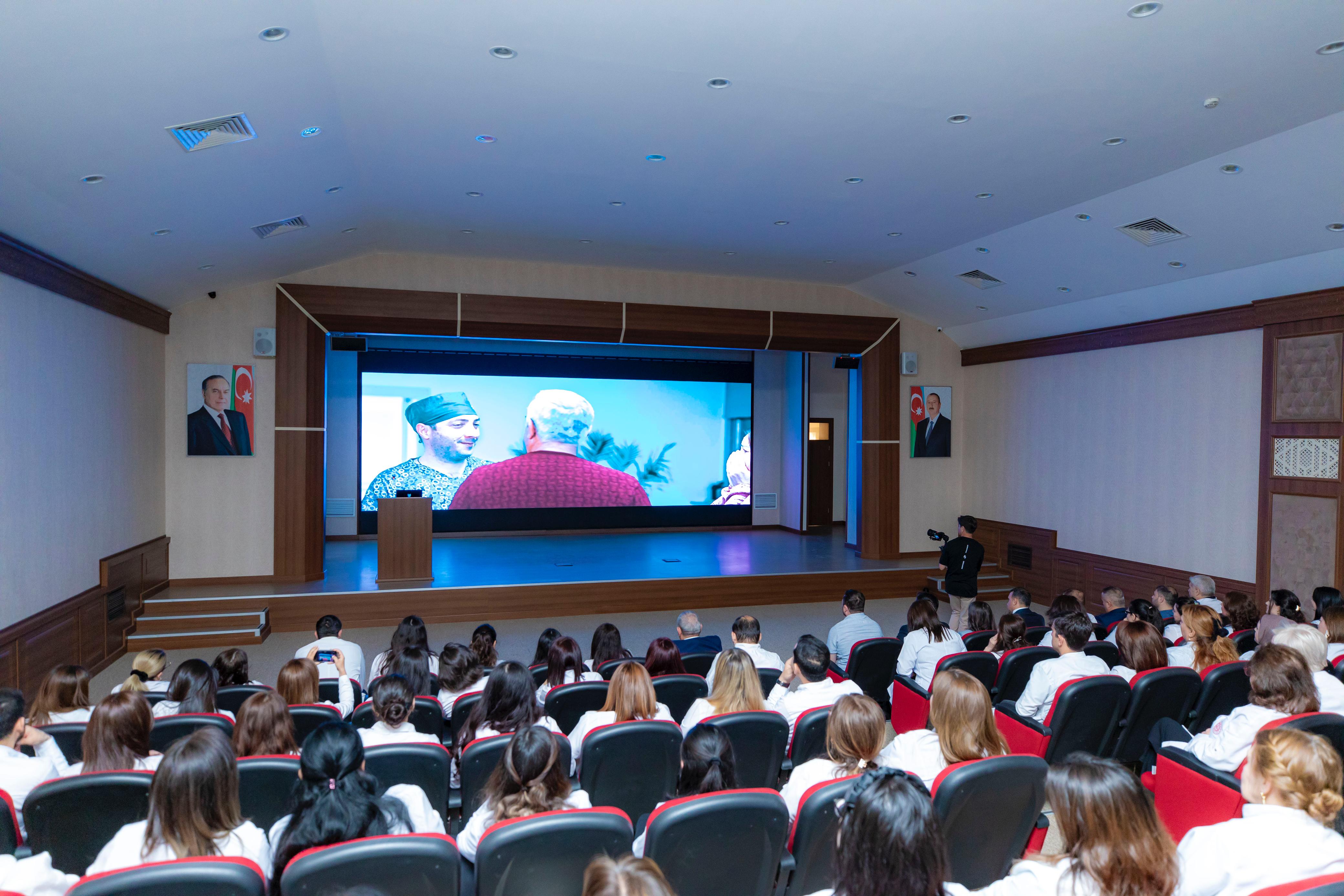 a group of people sitting in a room with a large screen