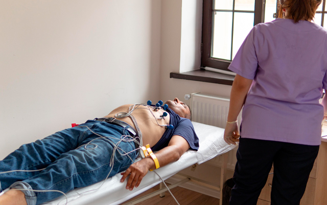 A patient lies on a medical bed with monitoring equipment attached, while a healthcare worker stands nearby.