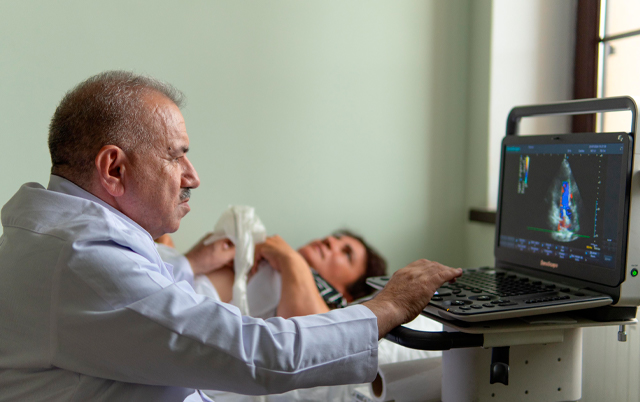 A doctor examines a patient's ultrasound results on a computer while the patient lies on a bed, looking concerned.
