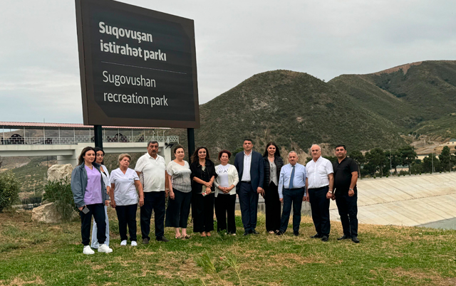A group of people stands in front of a sign for Sugovushan Recreation Park, with hills in the background.