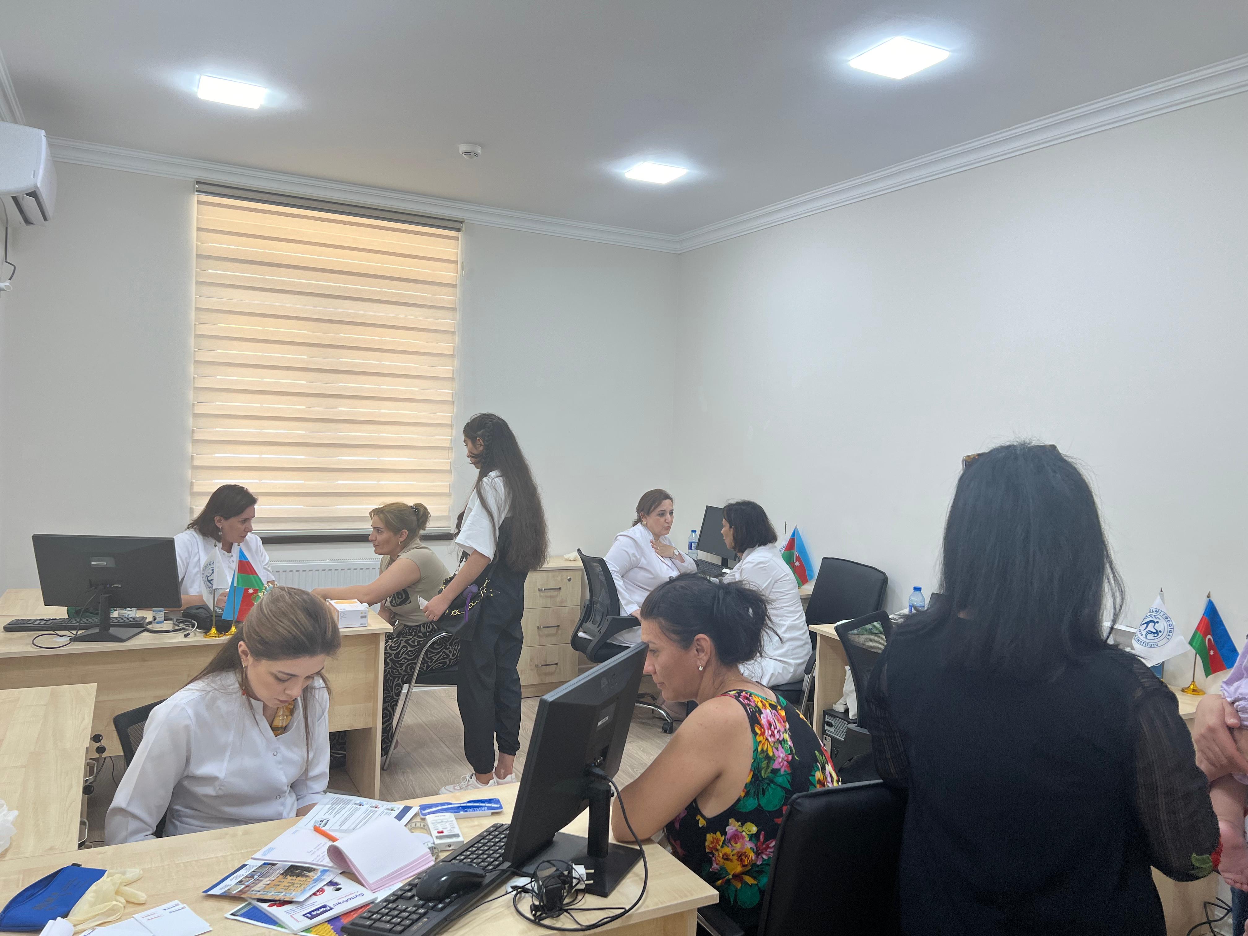 An office setting with several people engaged in discussions, computers on desks, and flags displayed.