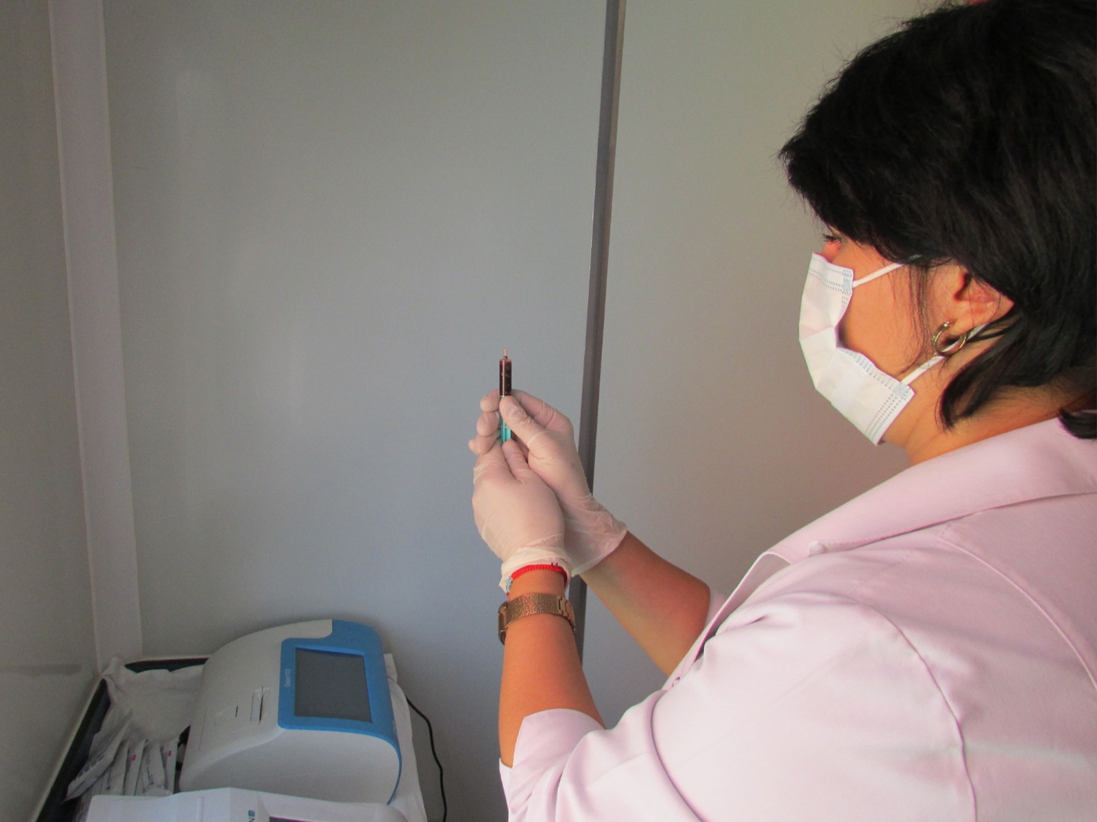 A healthcare professional in gloves holds a syringe, preparing for a procedure, with medical equipment in the background.