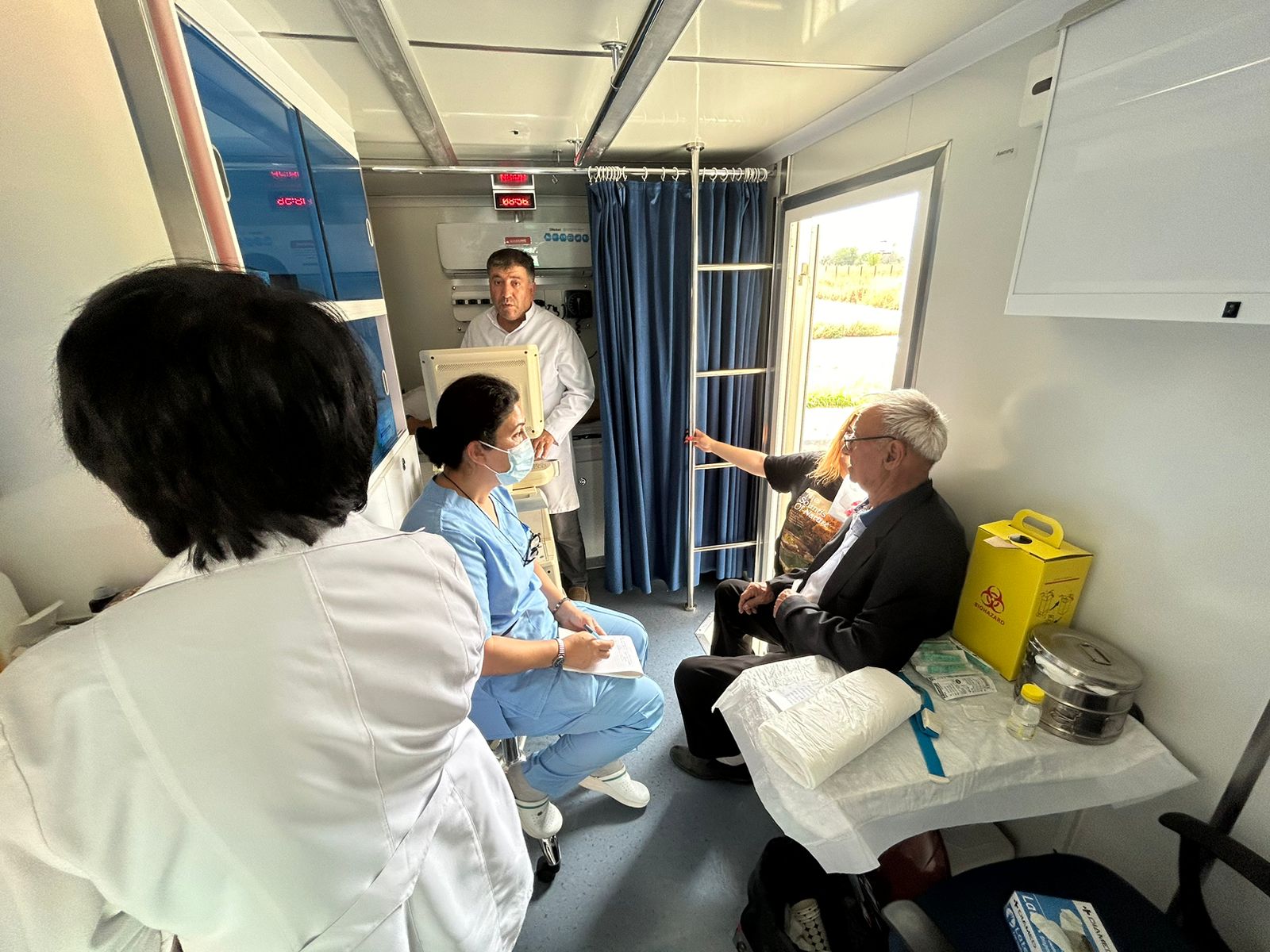 A medical setting with healthcare professionals attending to a patient. Equipment and supplies are visible in the background.