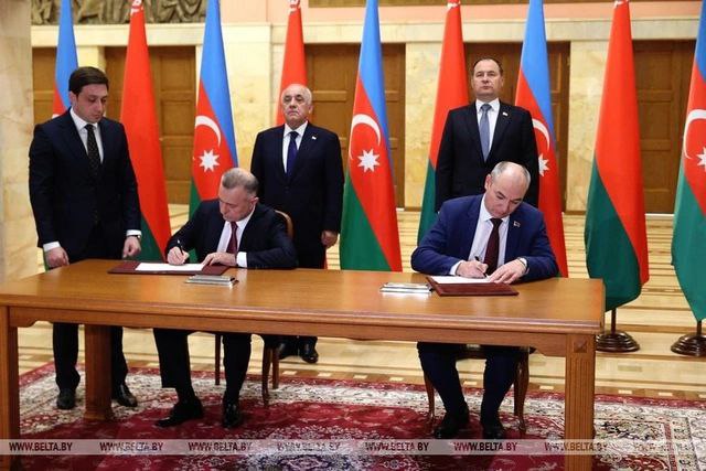 Two officials are signing documents at a table, with flags of Azerbaijan in the background and other officials standing behind them.