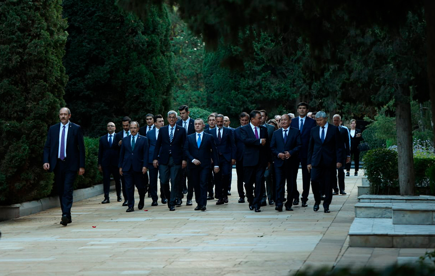 A group of men in suits walking together along a pathway lined with trees.