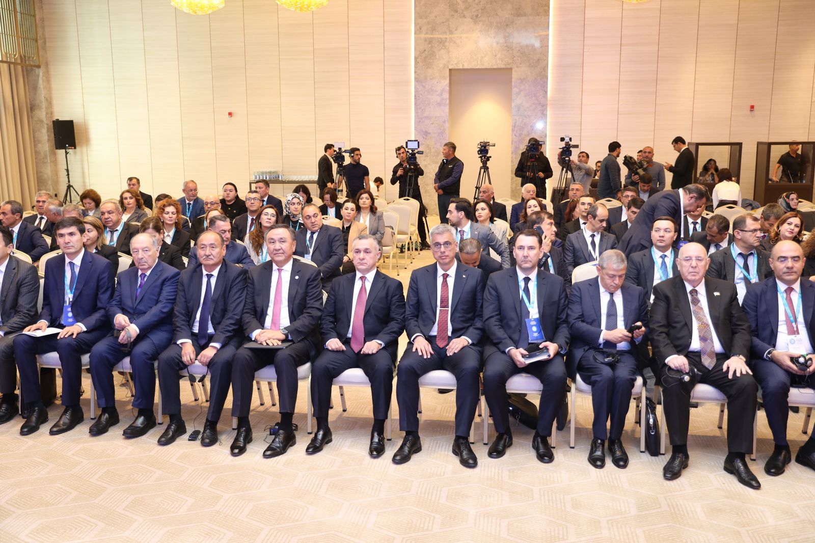 A large group of people seated in a conference setting, with several individuals in formal attire at the front.