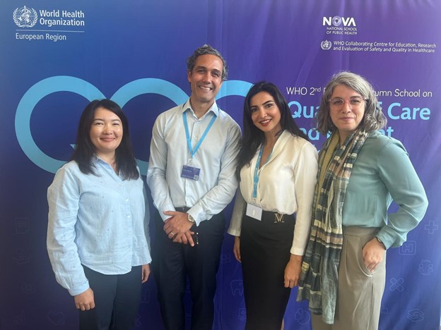 Four individuals pose together in front of a World Health Organization backdrop, promoting a quality care event.