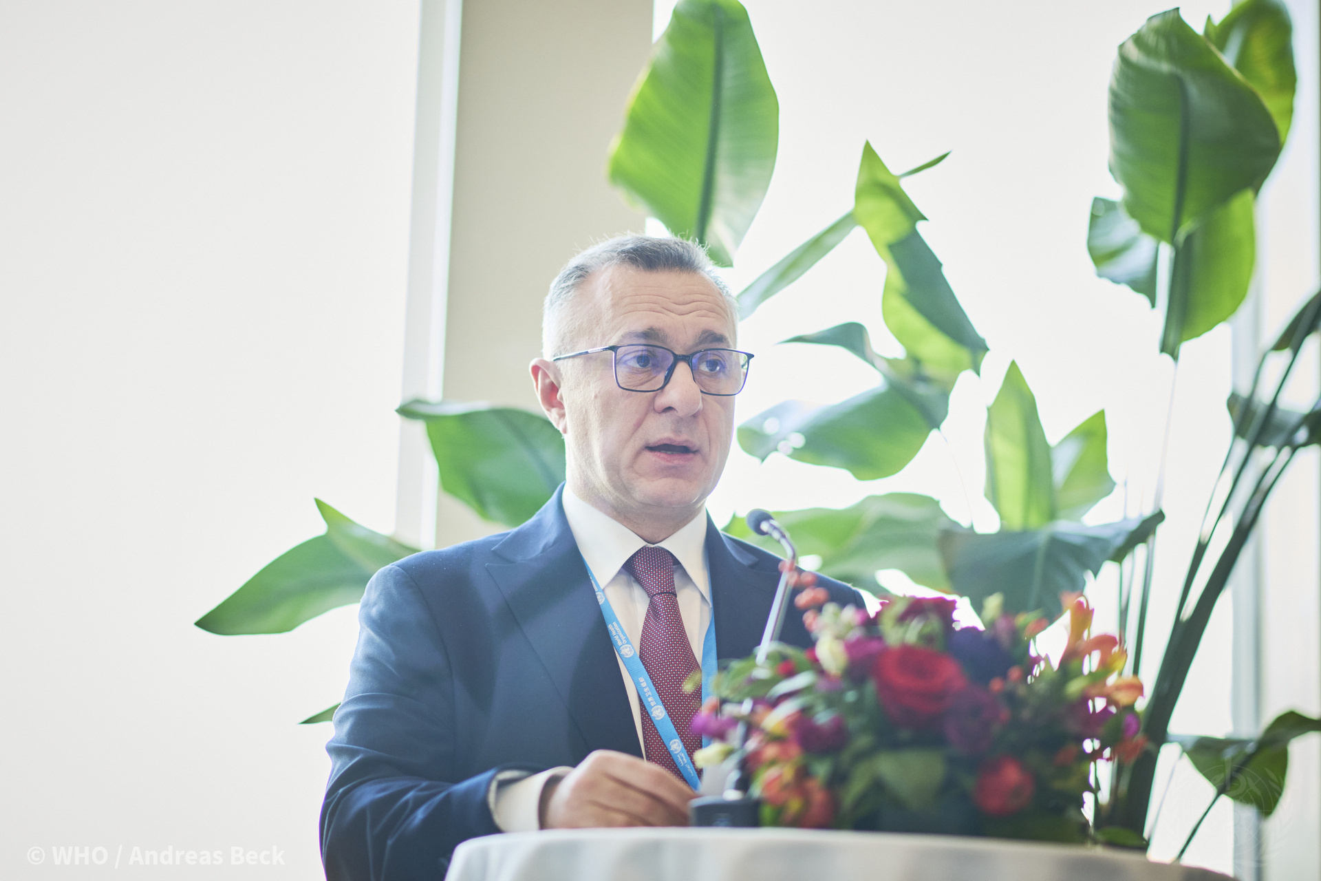 a man in a suit sitting at a table with a bouquet of flowers