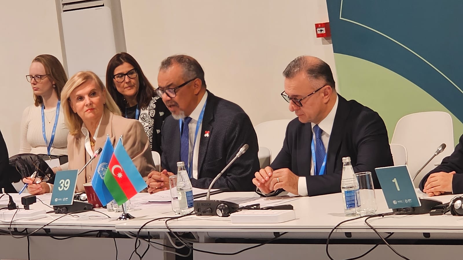 A group of professionals at a conference table, discussing with flags of Azerbaijan and another country visible.