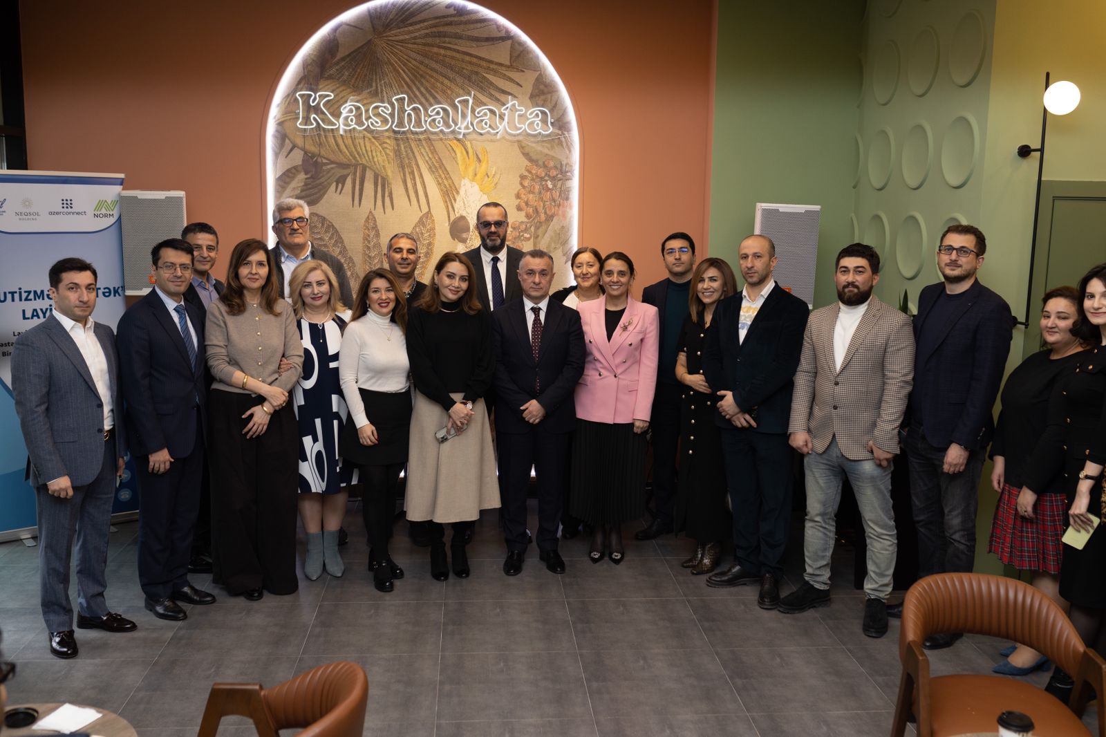 A group of professionals poses together in a modern venue, featuring a decorative wall with the name "Kashalata."