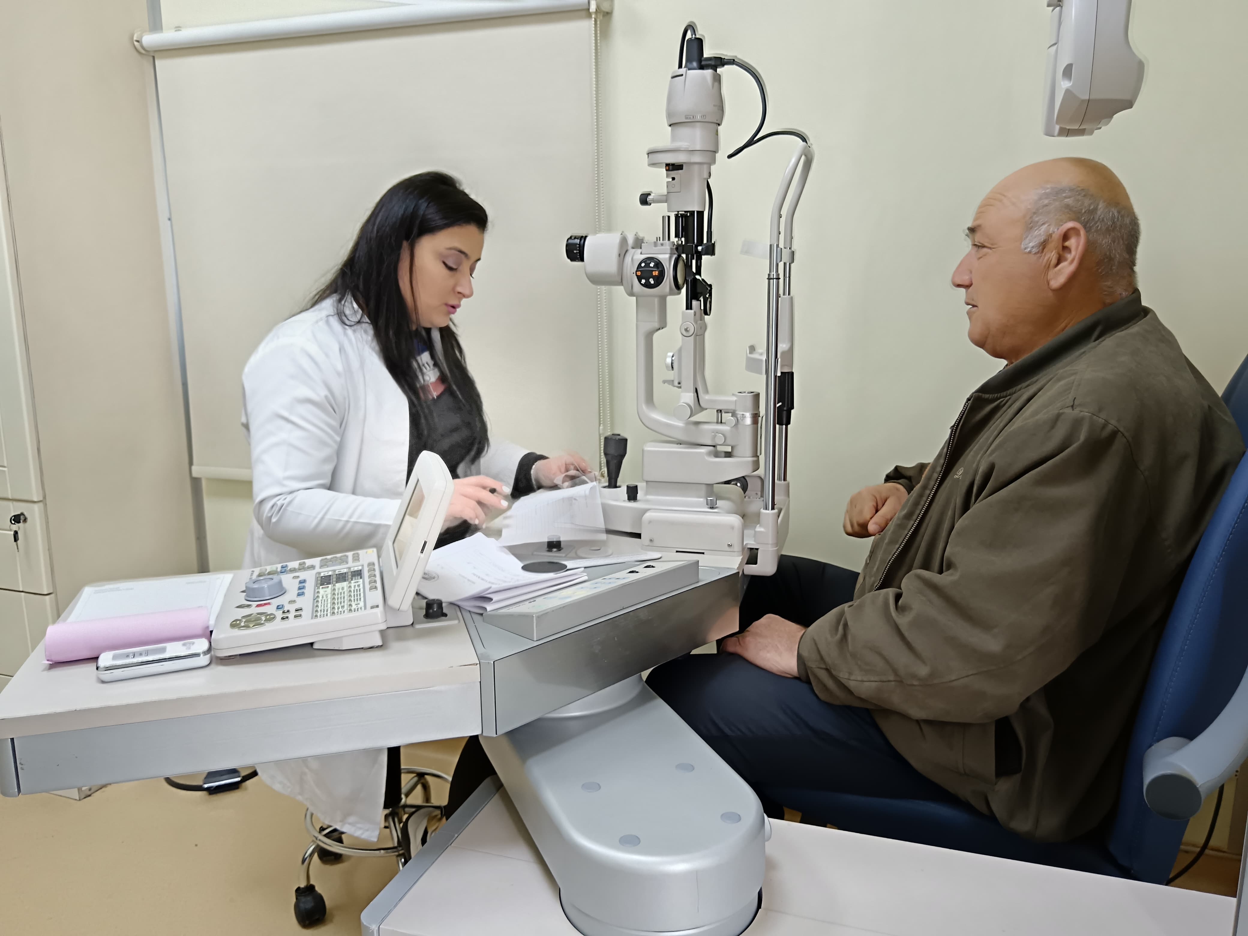 A healthcare professional examines a patient using an eye examination machine in a clinical setting.