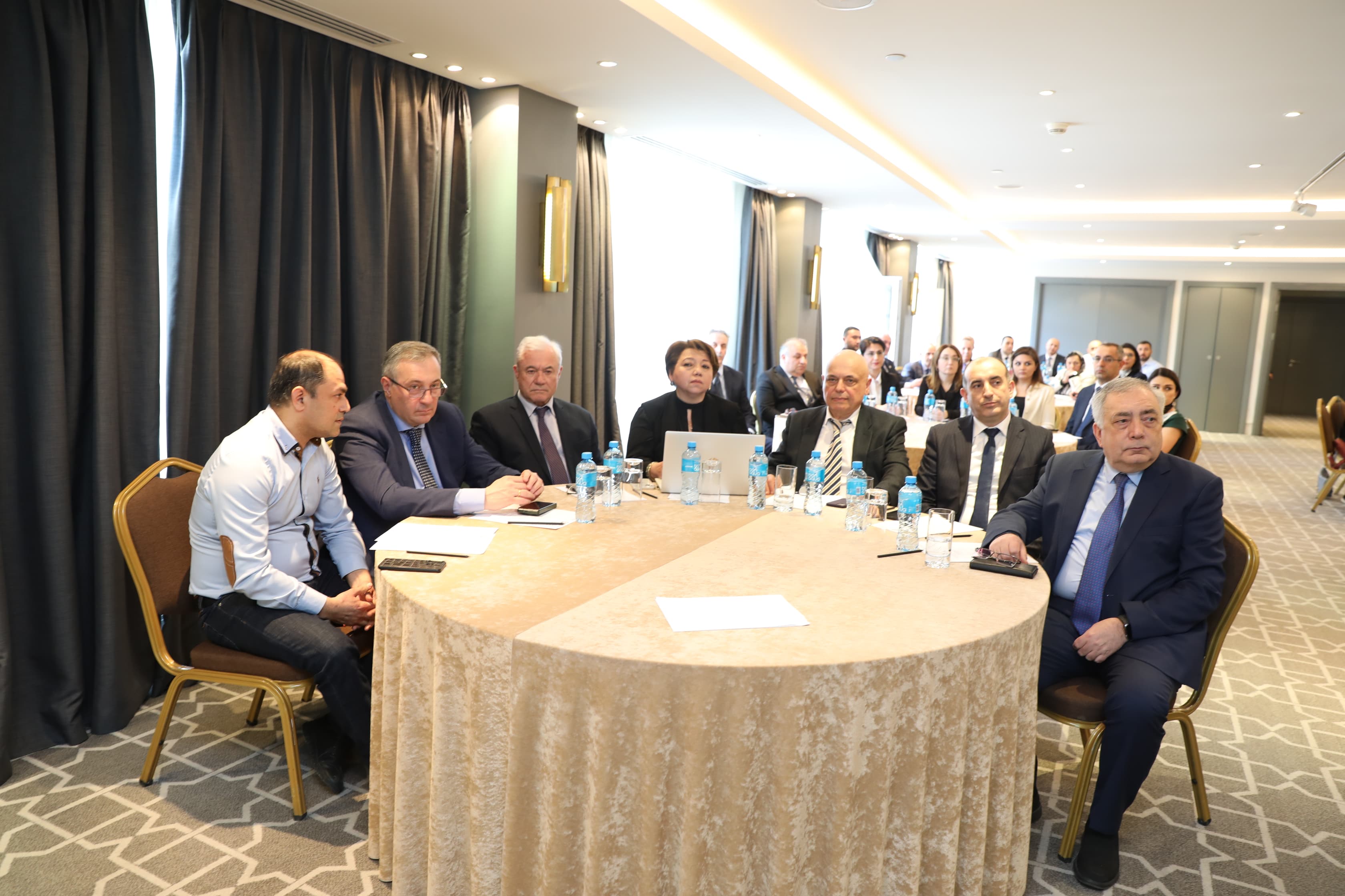 A group of people seated around a table in a conference room, engaged in discussion.