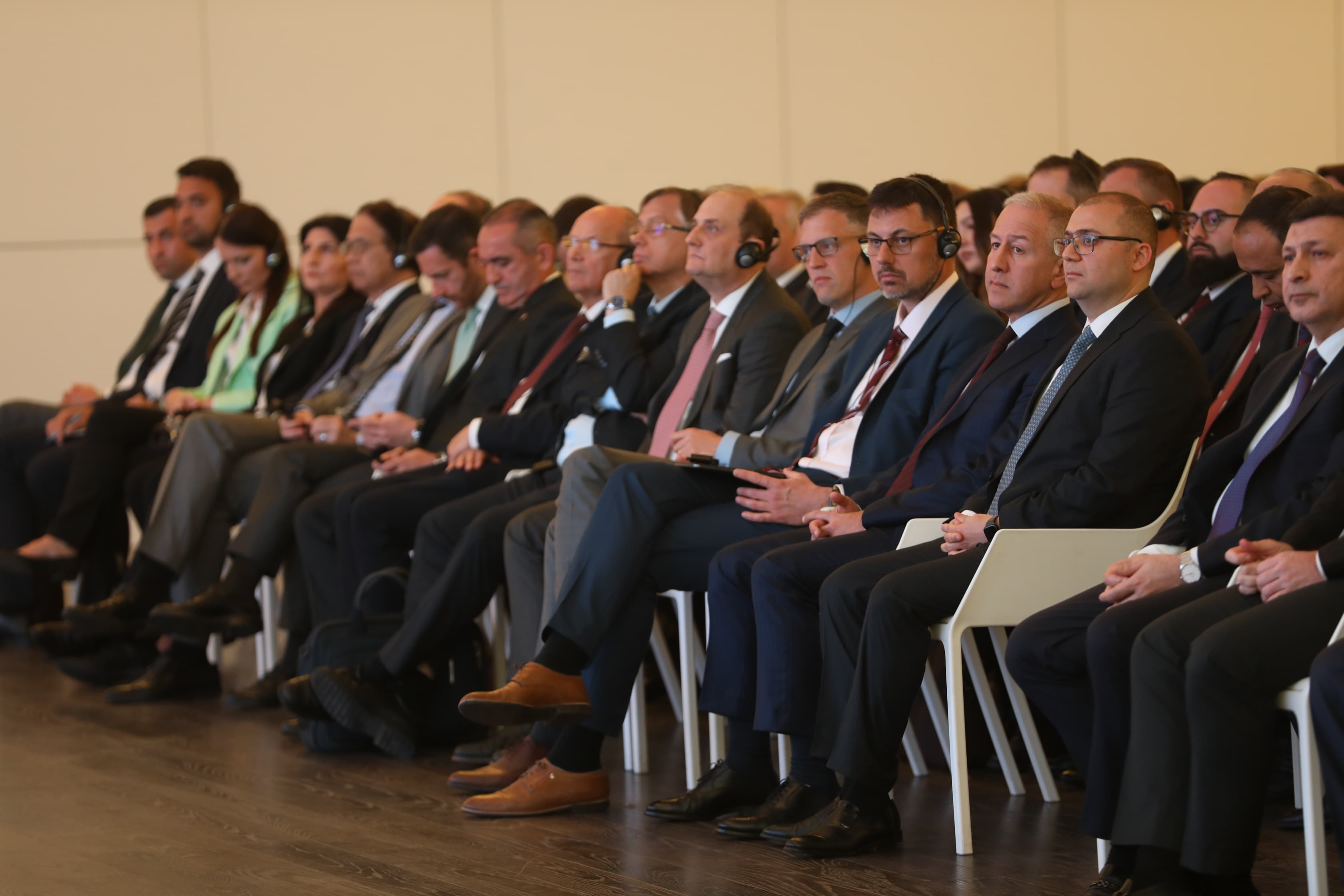 A group of people in formal attire seated in a conference setting, attentively listening.