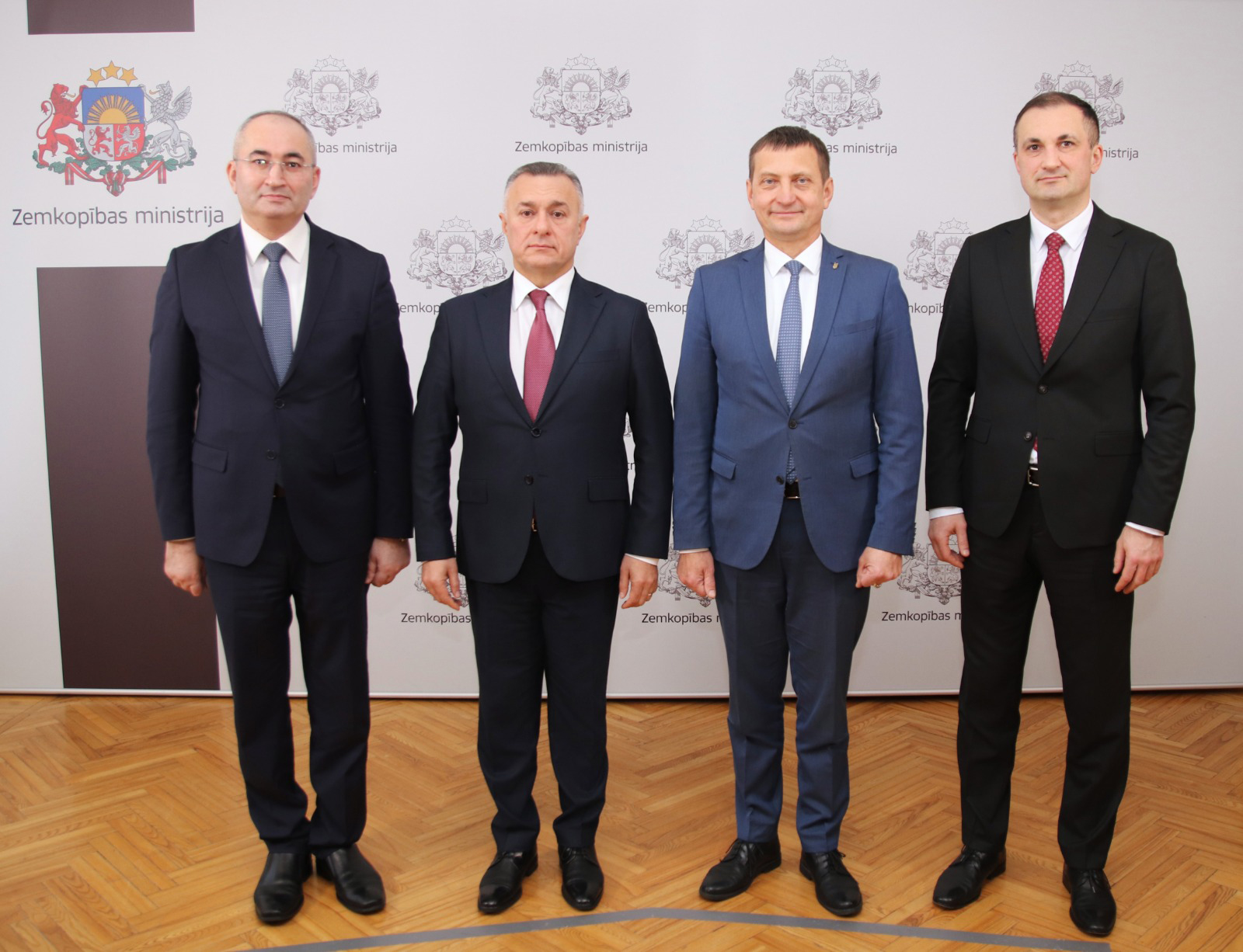 Four men in formal attire stand together in front of a backdrop featuring the Zemkopibas ministry logo.